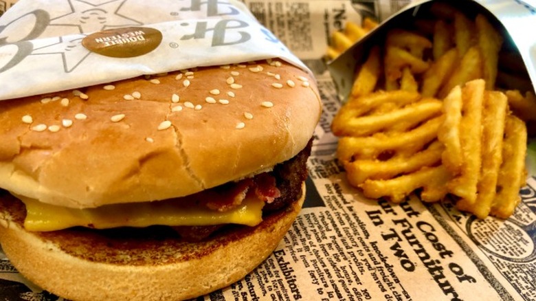 A bacon cheeseburger sits next to waffle fries at Carl's Jr.