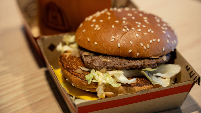 A Big Mac is sloppily put together inside a cardboard McDonalds box