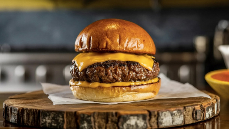 A cheeseburger sits on a wooden plate