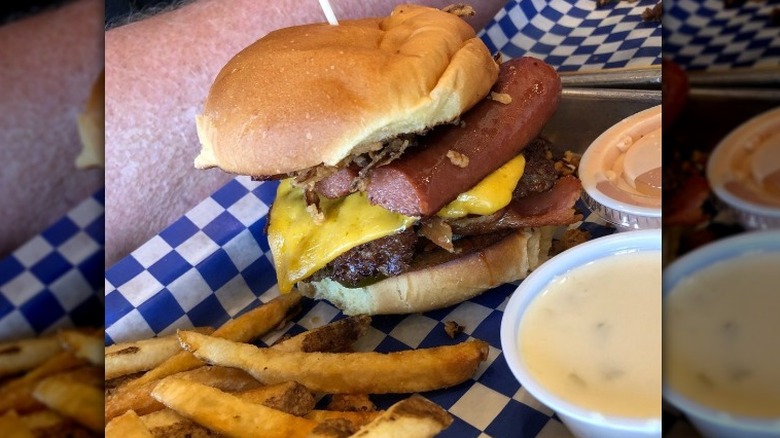 A cheeseburger with smoked sausage sits on a paper wrapper next to fries and sauces at a Mooyah Burgers restaurant