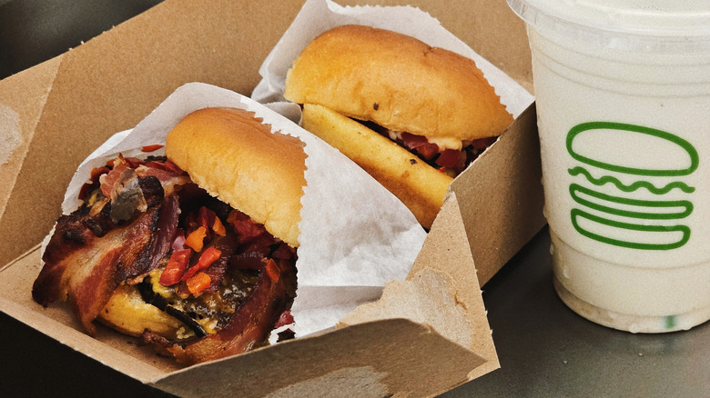 Two bacon burgers sit next to a milkshake with a Shake Shack logo