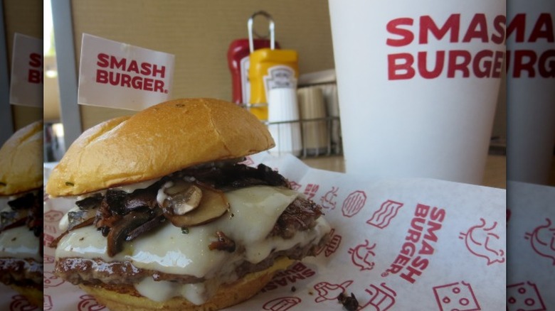 A mushroom cheeseburger sits next to a drink in a Smash Burger restaurant