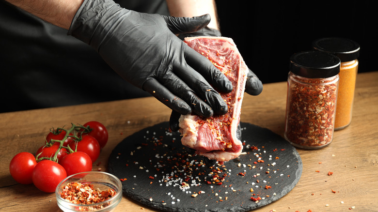 A chef massages a steak with jarred steak rub.