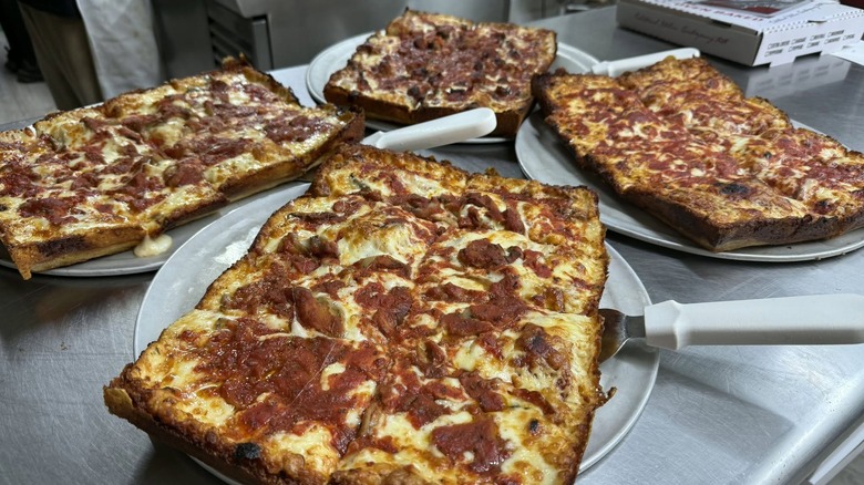 Four Detroit-style pizzas on silver trays.