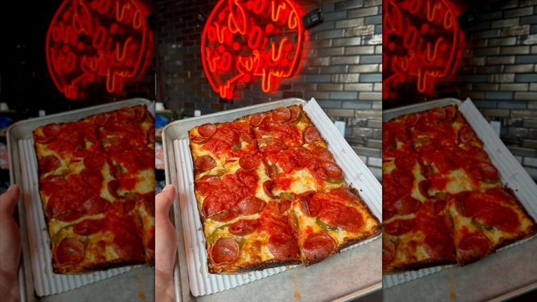 Detroit-style pizza on a silver pan in front of red neon sign.