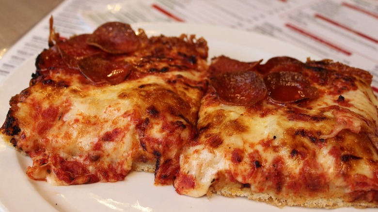 Close-up shot of two slices of Detroit-style pizza on a white plate.