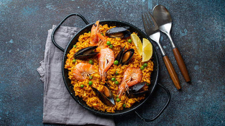 traditional paella in pan next to serving utensils