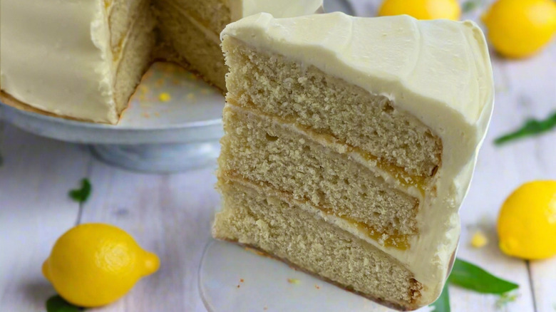 A slice of Daisy Cakes' gluten-free lemon cake sits on a wooden surface surrounded by lemons