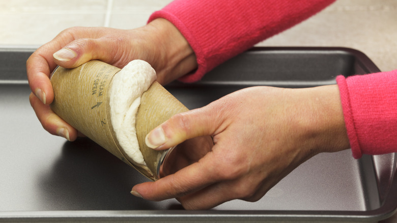 woman opening can of biscuit dough over a baking sheet