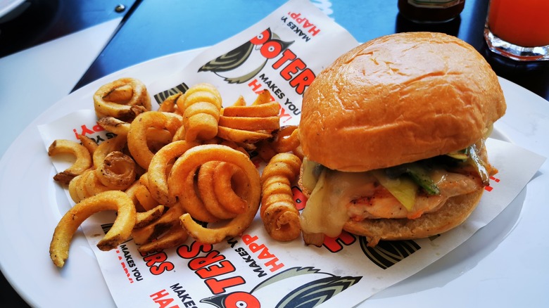 A chicken sandwich and curly fries on a plate with Hooters branded parchment paper