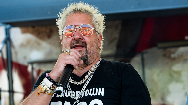 Guy Fieri with sunglasses on holding a microphone