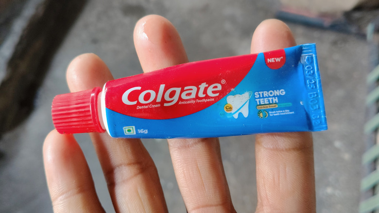 A hand holds a small tube of Colgate toothpaste.