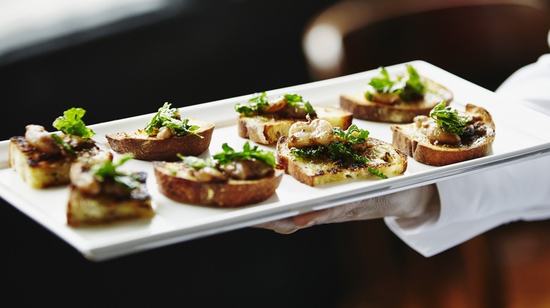 A sever presenting a plate of appetizers with bread, greens, and protein