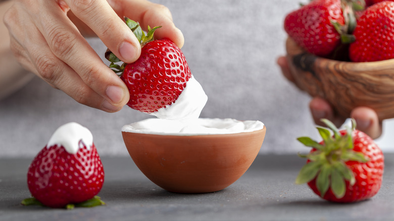 Strawberries are being dipped in white cream.