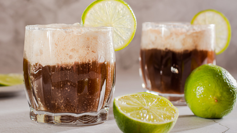 Homemade dirty sodas in two glasses with cream and lime wedges