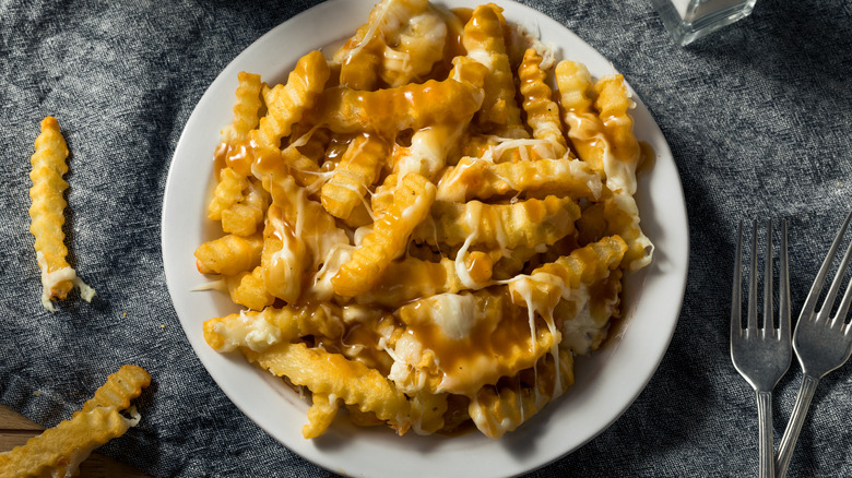 Disco fries on a plate with salt and pepper and forks on the surface around it