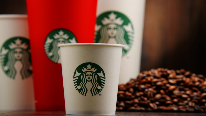 many different Starbucks cups in different sizes next to a pile of coffee beans