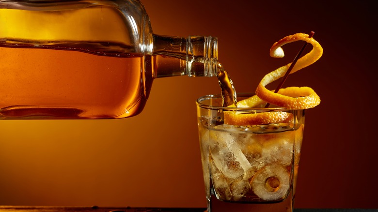 Bourbon being poured into a glass with ice and a lemon garnish