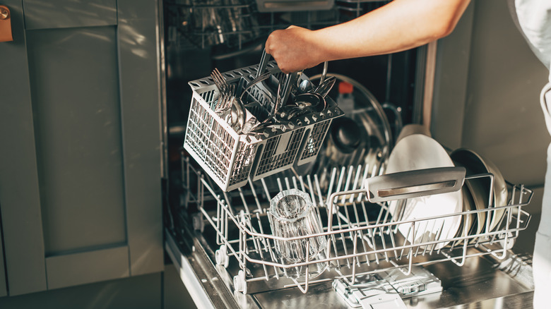 Person removing full silverware caddy from dishwasher