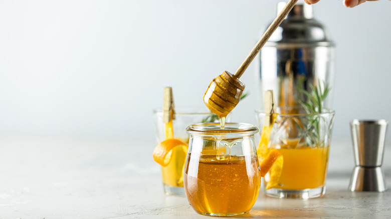 A jar of honey next to two bourbon cocktails