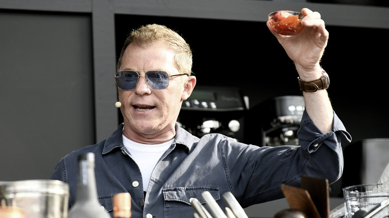 Bobby Flay holds up a small bowl of sauce on stage at an event.