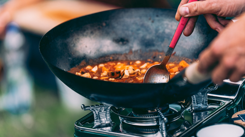 person cooking curry in wok outdoors