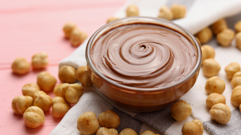 Nutella in a small glass bowl with shelled hazelnuts around it