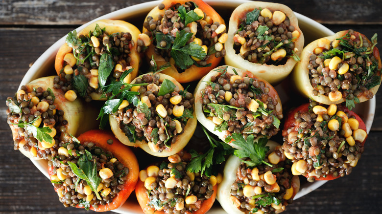A white bowl of red and yellow bell peppers stuffed with lentils, quinoa, corn and black beans