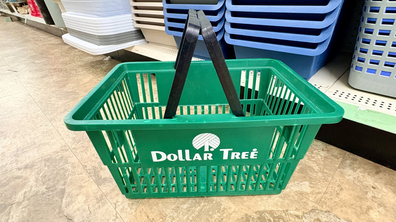 A green Dollar Tree shopping basket sits on the floor of a store.