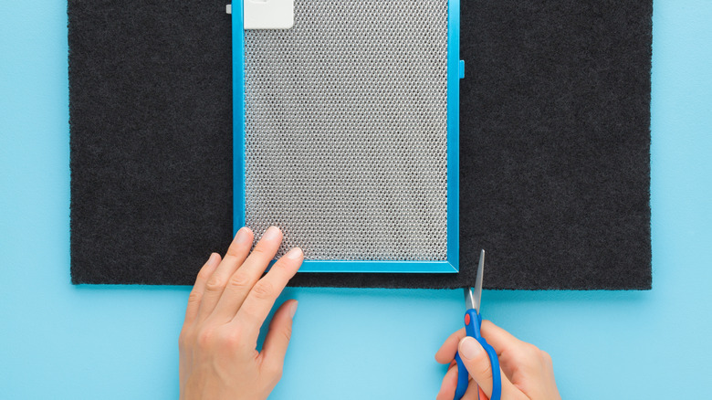 A person cuts a charcoal filter to fit into a metal screen