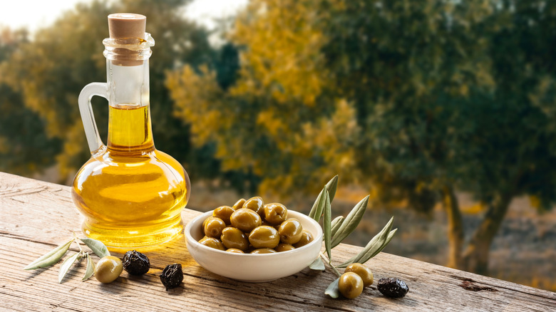 Olives in a bowl next to olive oil on a wooden table
