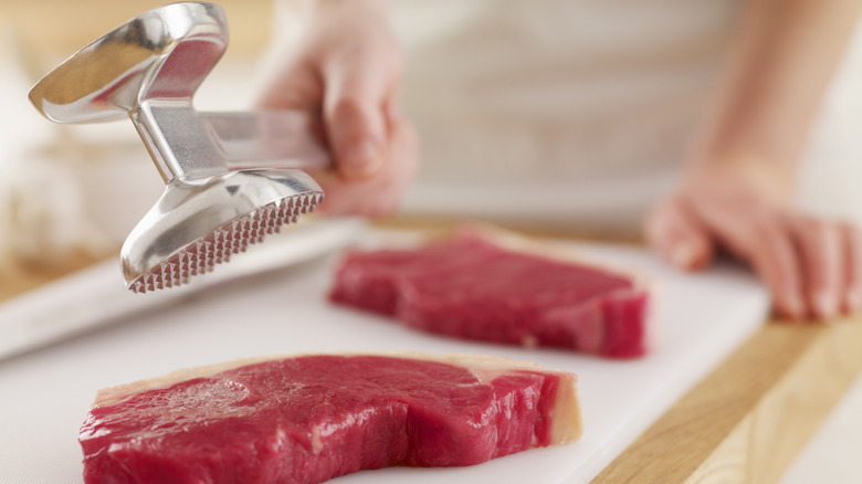 Person tenderizing a steak with a meat mallet.