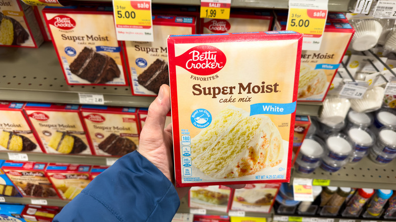 Hand holding boxed cake mix in grocery store aisle