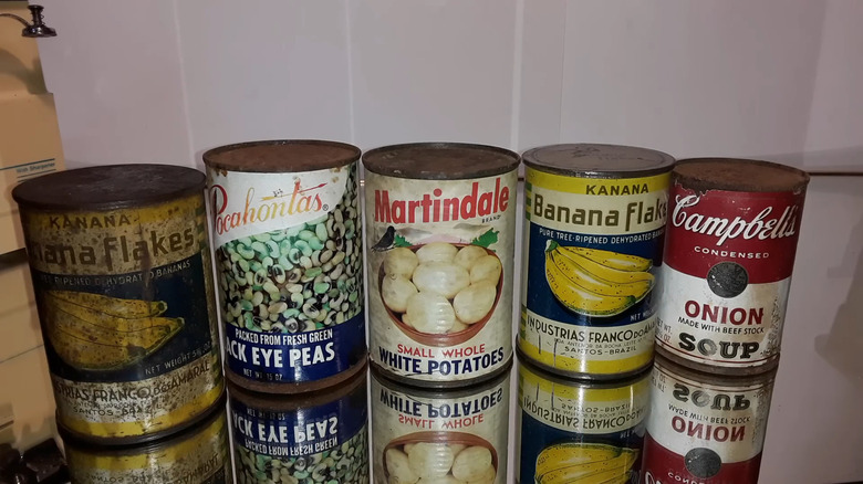 Rusty cans of fruit, vegetables, and soup sit on a glass table.