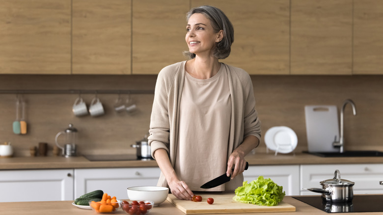 A happy woman chops vegetables on a cutting board