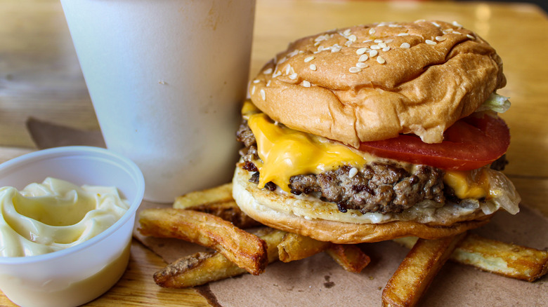 A Five Guys cheeseburger, french fries, and plastic container of mayonnaise sit on a table