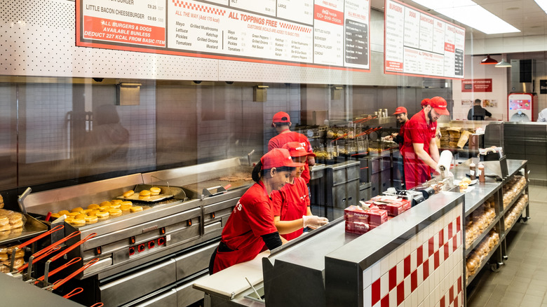 A group of workers at a Five Guys stand behind a counter preparing burgers