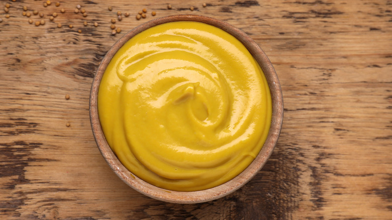 wooden bowl of mustard sauce with seeds on the wooden countertop