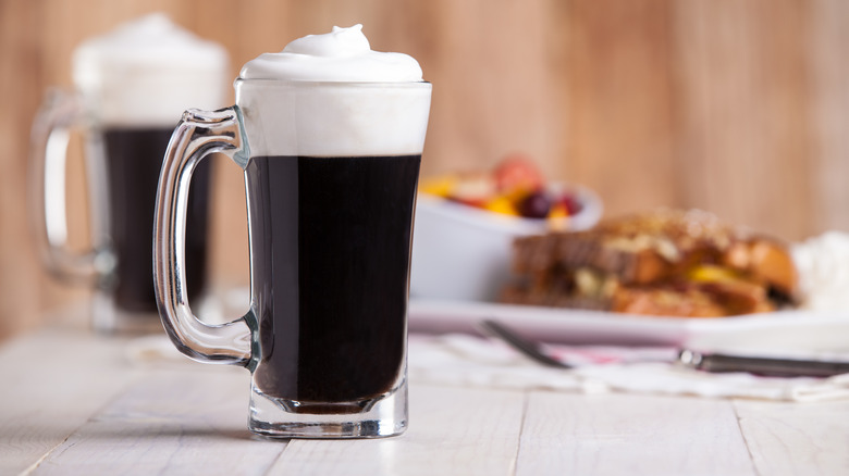 2 glass mugs of Irish coffee with breakfast in background