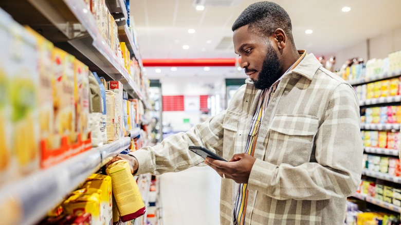 A customer checking his phone while they peruse an item on a shelf.