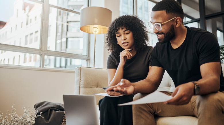 Two people excitedly looking at a laptop screen while taking notes.