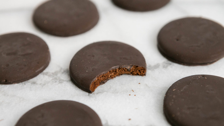 Closeup of several Girl Scouts Thin Mint chocolate-covered cookies scattered on a white surface, with a bite out of one