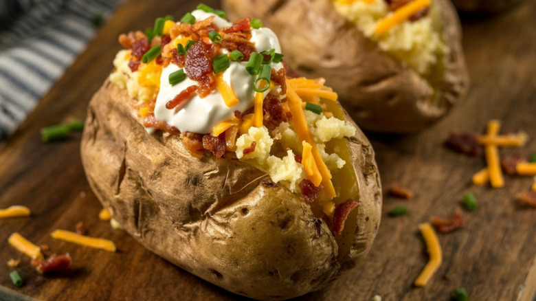 A loaded, baked russet potato topped with sour cream, shredded cheese, chopped scallions, and bacon