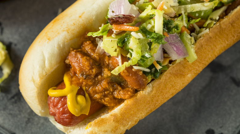 A hot dog is topped with coleslaw, chili, and mustard