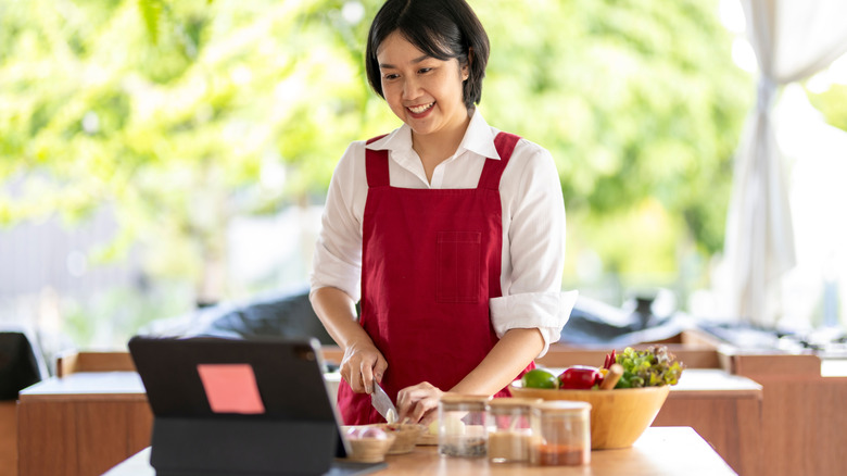 A home cook prepares a meal while consulting a tablet