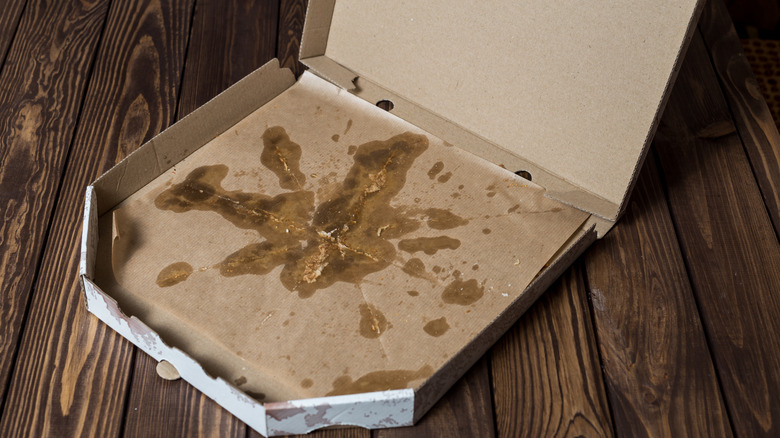 An empty, greasy pizza box sits on a wooden surface.