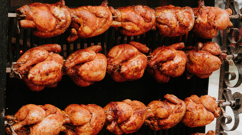 Rows of whole rotisserie chickens on spits
