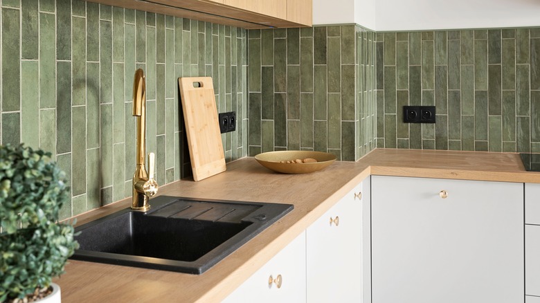 A kitchen counter with green tiled backsplash