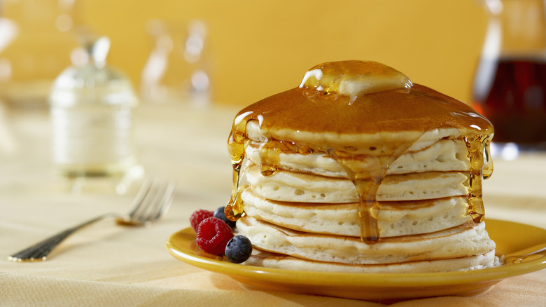 Stack of pancakes with maple syrup, butter, and berries.