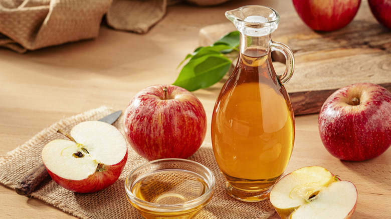 A bottle of homemade apple cider vinegar on a burlap table mat next to apples and a paring knife